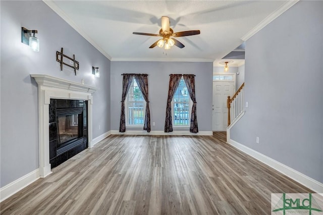 unfurnished living room featuring a tiled fireplace, wood finished floors, stairway, crown molding, and baseboards