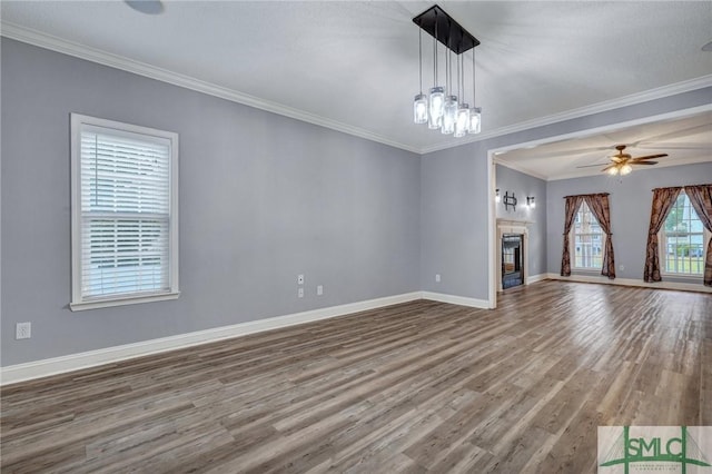 unfurnished living room with ornamental molding, ceiling fan with notable chandelier, wood finished floors, a fireplace, and baseboards