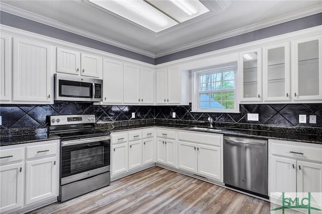 kitchen with light wood-style flooring, a sink, stainless steel appliances, dark stone counters, and white cabinets