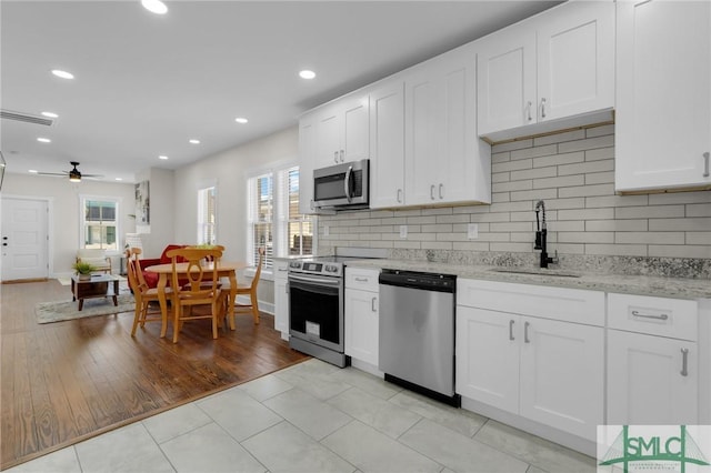 kitchen featuring a sink, backsplash, white cabinetry, stainless steel appliances, and light stone countertops