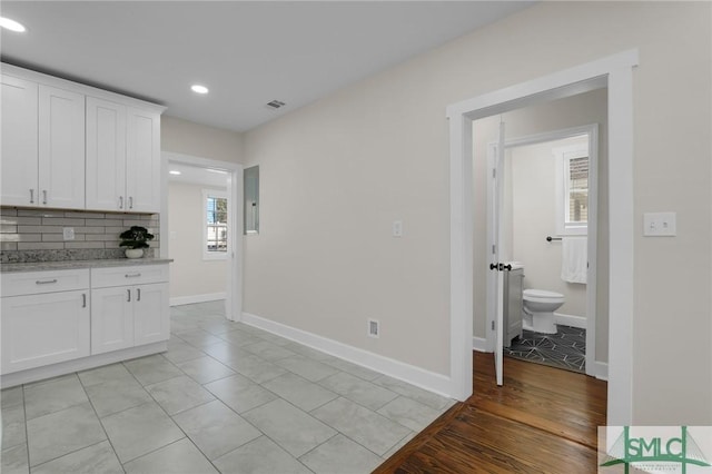 kitchen featuring visible vents, baseboards, backsplash, and white cabinetry