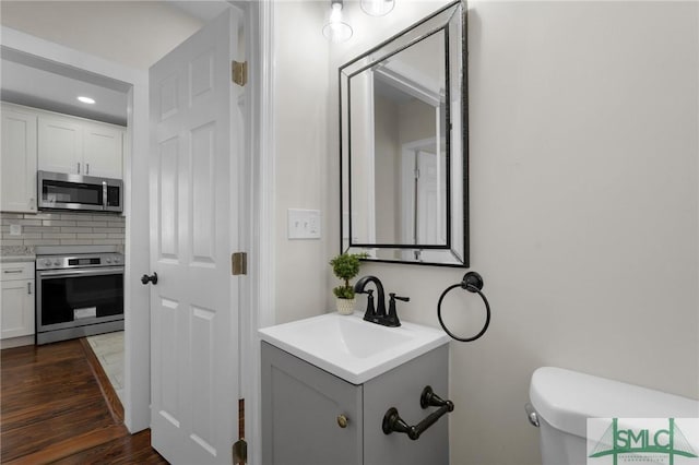 half bathroom with tasteful backsplash, toilet, vanity, and wood finished floors