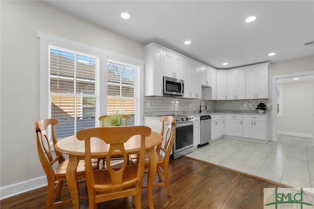 kitchen with light countertops, light wood-style floors, appliances with stainless steel finishes, white cabinetry, and backsplash