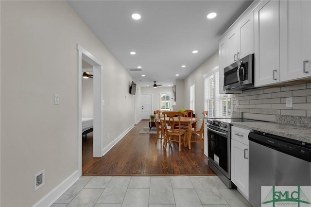 kitchen with light tile patterned floors, ceiling fan, appliances with stainless steel finishes, white cabinetry, and backsplash