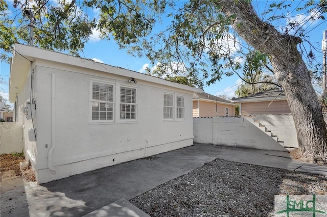 view of side of property featuring a patio area, fence, and stucco siding