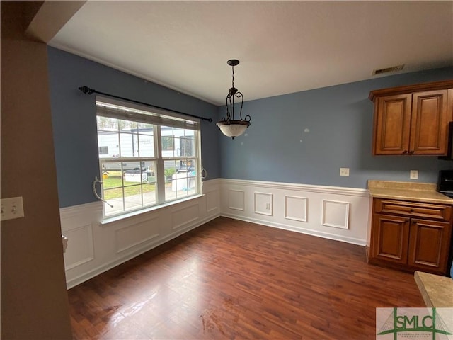 unfurnished dining area with visible vents, dark wood-type flooring, and a wainscoted wall