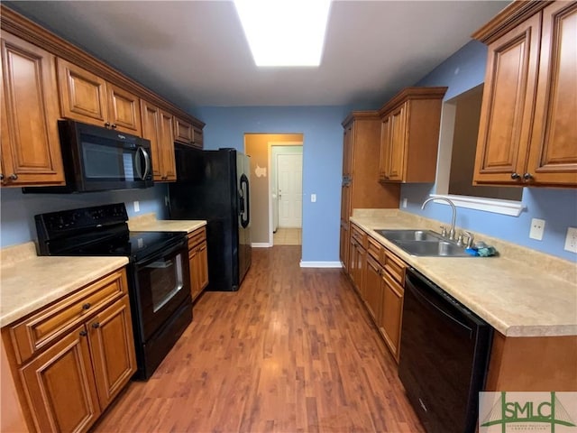 kitchen with black appliances, a sink, light wood-style floors, brown cabinetry, and light countertops