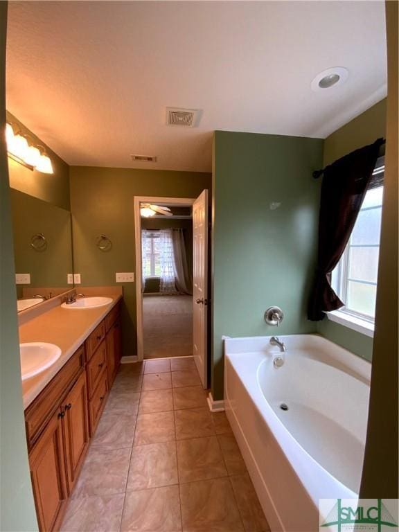 full bath featuring visible vents, double vanity, a sink, tile patterned flooring, and a garden tub