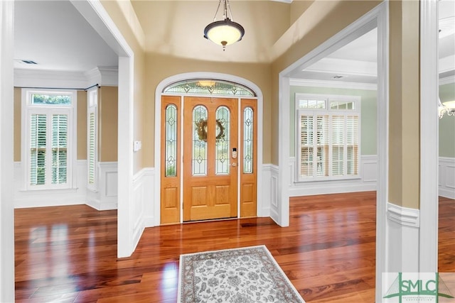 entrance foyer with crown molding, wood finished floors, and a wainscoted wall