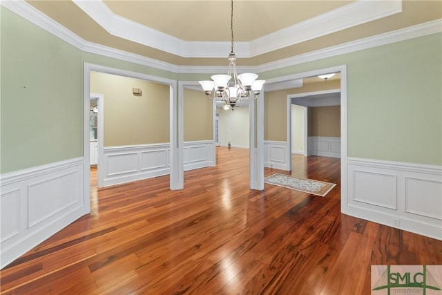 unfurnished dining area with a wainscoted wall, hardwood / wood-style flooring, crown molding, a raised ceiling, and a chandelier