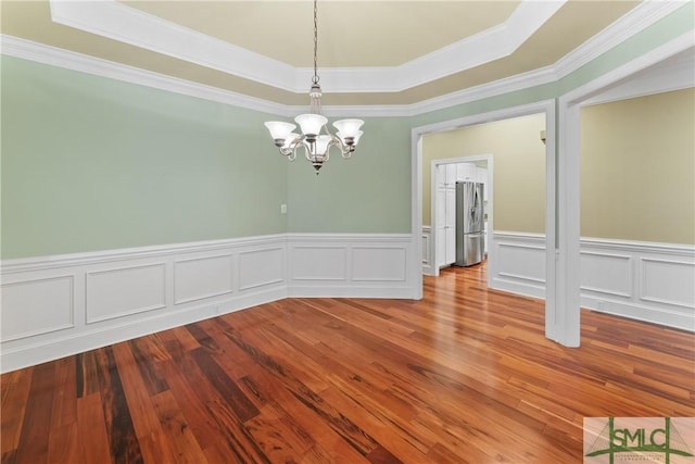 unfurnished dining area featuring a raised ceiling, ornamental molding, wood finished floors, and a chandelier