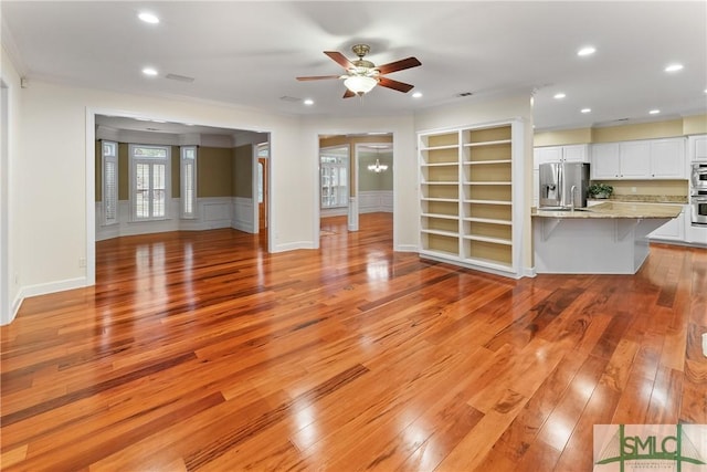 unfurnished living room with recessed lighting, ceiling fan with notable chandelier, crown molding, and light wood-style floors