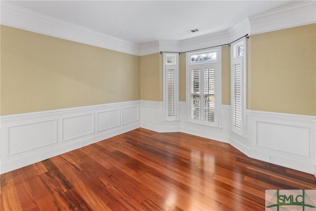 unfurnished room with wood finished floors, visible vents, and ornamental molding