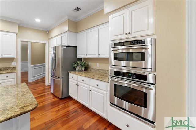 kitchen featuring visible vents, ornamental molding, appliances with stainless steel finishes, white cabinets, and light wood finished floors