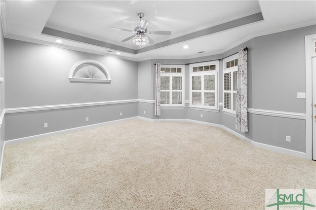 carpeted empty room featuring ceiling fan, a tray ceiling, baseboards, and ornamental molding