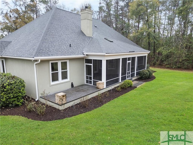 rear view of property featuring roof with shingles, a sunroom, stucco siding, a chimney, and a lawn