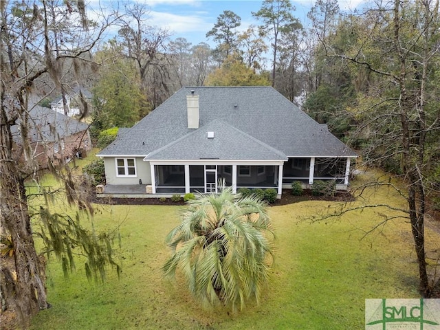 back of house with a chimney, a lawn, a shingled roof, and a sunroom