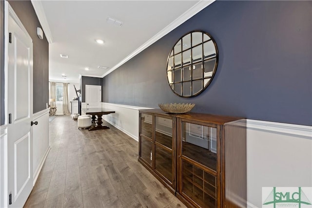 corridor with wood finished floors, visible vents, and ornamental molding