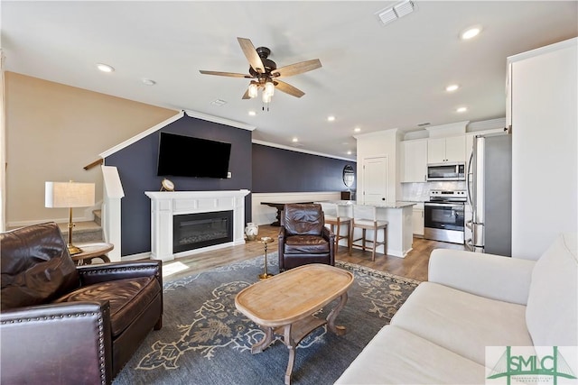 living room with wood finished floors, visible vents, recessed lighting, ceiling fan, and crown molding