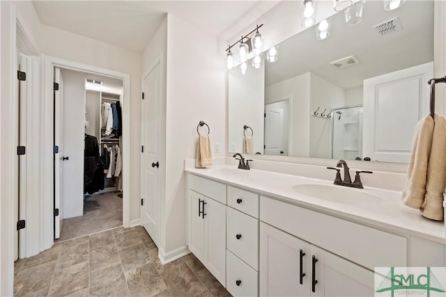 full bathroom with double vanity, a stall shower, a walk in closet, and a sink