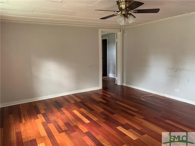 empty room featuring dark wood-type flooring, a ceiling fan, and baseboards