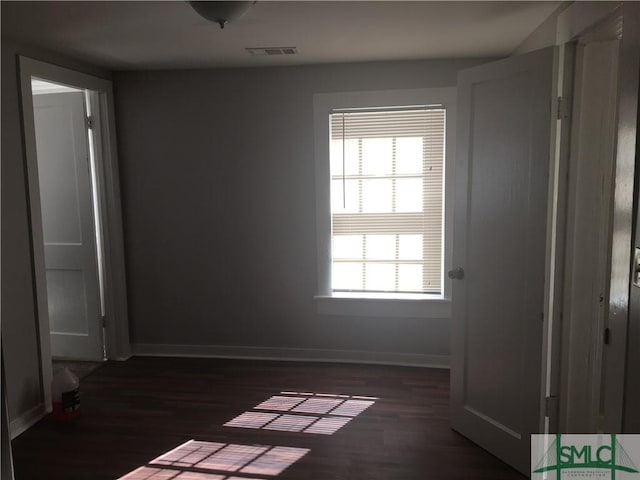 spare room featuring dark wood finished floors, visible vents, and baseboards