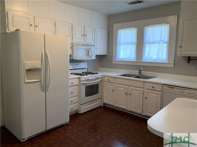 kitchen with dark floors, light countertops, white cabinets, white appliances, and a sink