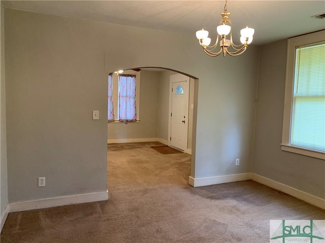 spare room with a wealth of natural light, arched walkways, carpet, and an inviting chandelier