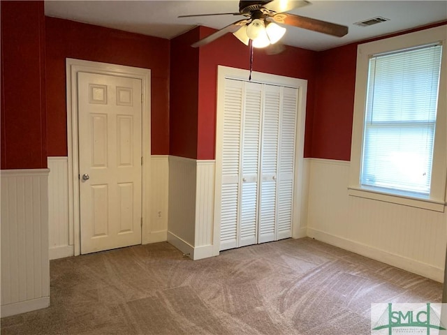 unfurnished bedroom featuring carpet, visible vents, a closet, and wainscoting