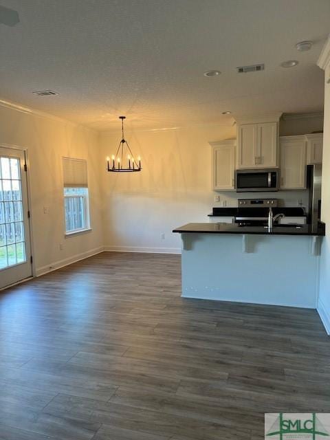 kitchen with dark countertops, a chandelier, dark wood finished floors, appliances with stainless steel finishes, and white cabinets