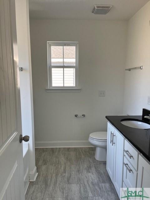 bathroom with vanity, toilet, baseboards, and visible vents