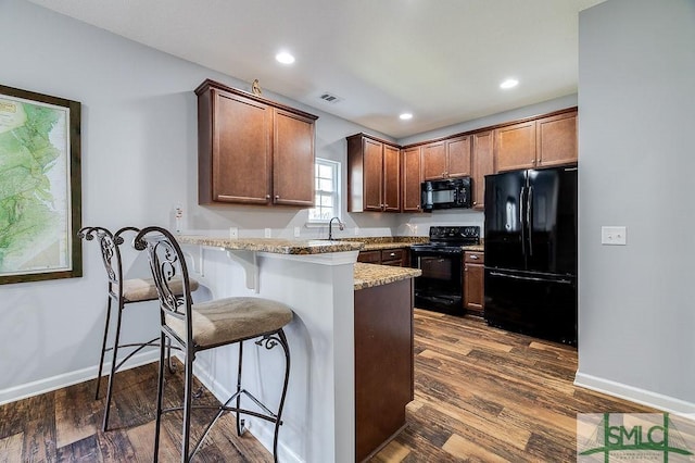 kitchen with dark wood-style floors, a peninsula, a sink, black appliances, and a kitchen bar