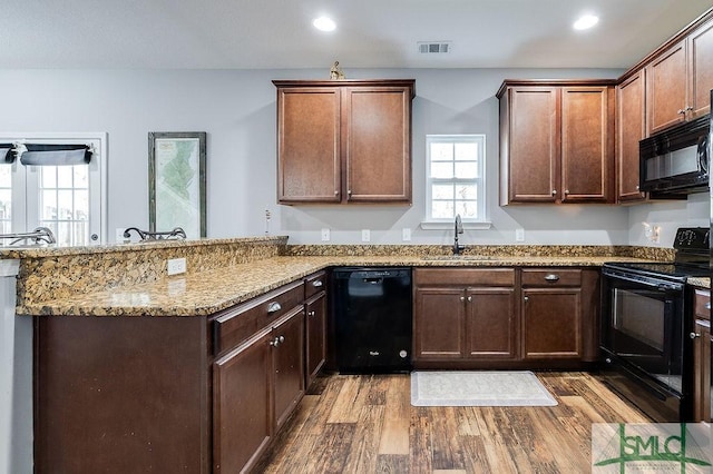 kitchen featuring wood finished floors, visible vents, a peninsula, a sink, and black appliances