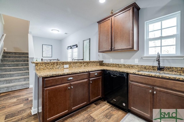 kitchen featuring light stone countertops, a peninsula, a sink, dark wood-type flooring, and black dishwasher