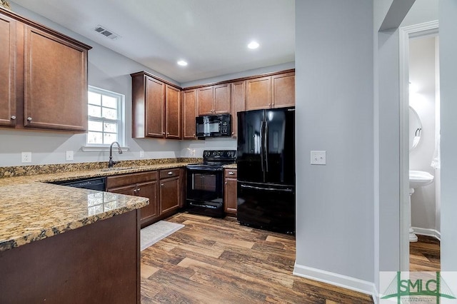 kitchen featuring light stone countertops, visible vents, dark wood-style flooring, a sink, and black appliances