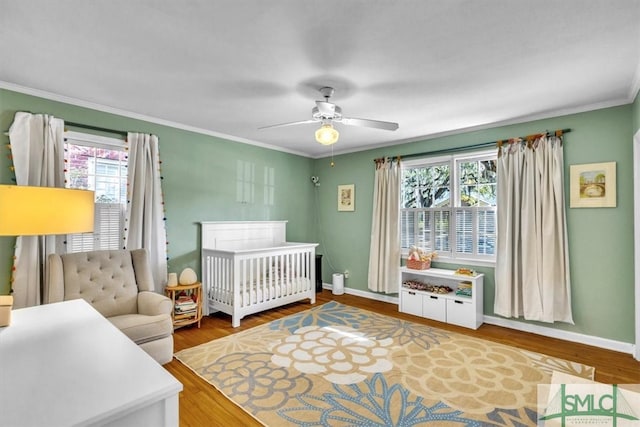 bedroom featuring a crib, crown molding, multiple windows, and wood finished floors