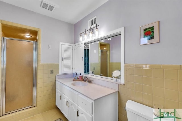 bathroom featuring visible vents, toilet, vanity, a stall shower, and tile walls