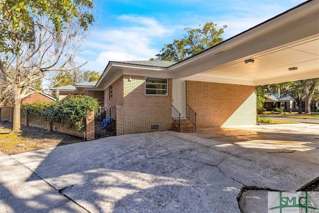 view of side of property with brick siding, an attached carport, entry steps, concrete driveway, and crawl space