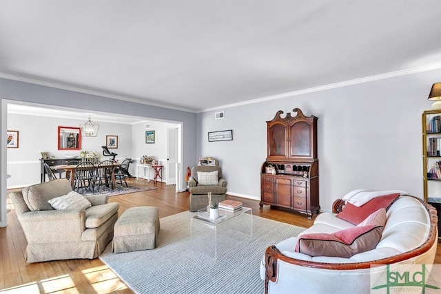 living area featuring baseboards, wood finished floors, visible vents, and ornamental molding