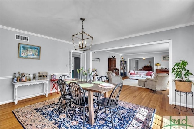 dining space with visible vents, crown molding, baseboards, an inviting chandelier, and wood finished floors