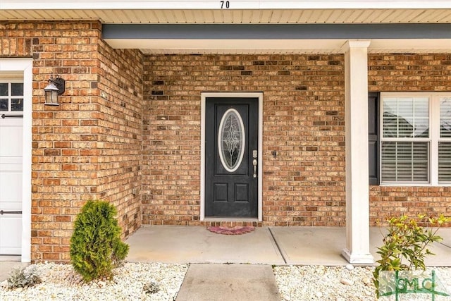 property entrance with brick siding, an attached garage, and a porch