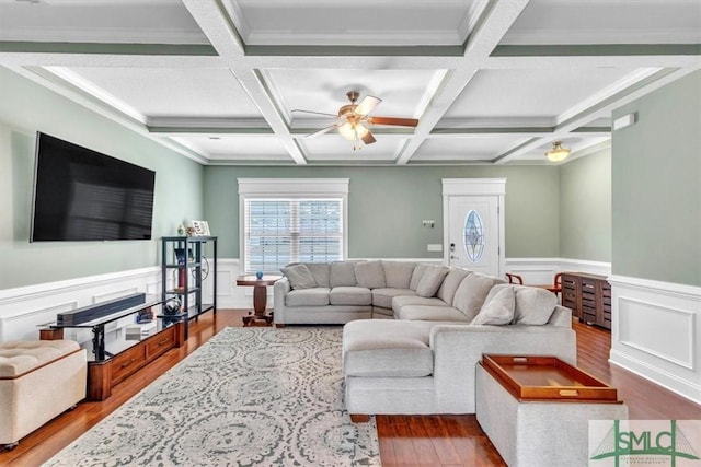 living area featuring beamed ceiling, a wainscoted wall, wood finished floors, and a ceiling fan