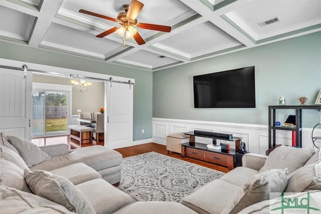 living room with visible vents, beam ceiling, ceiling fan with notable chandelier, wood finished floors, and a barn door