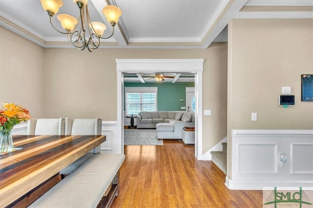 corridor featuring a wainscoted wall, crown molding, light wood-type flooring, and an inviting chandelier