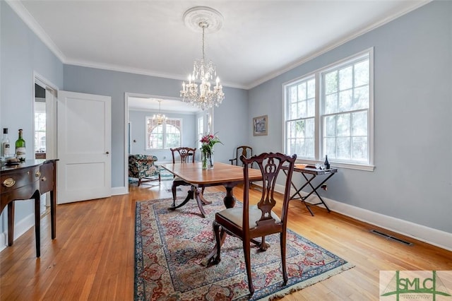 dining room featuring visible vents, crown molding, baseboards, light wood-style floors, and a notable chandelier