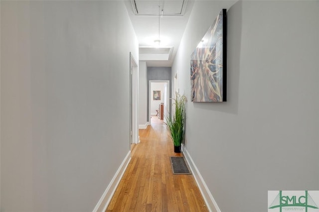 hall featuring light wood-type flooring, visible vents, baseboards, and attic access