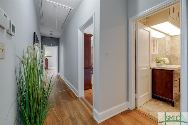 hallway with attic access, baseboards, light wood finished floors, and a sink