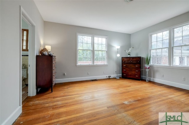 unfurnished bedroom featuring light wood-type flooring, multiple windows, and baseboards