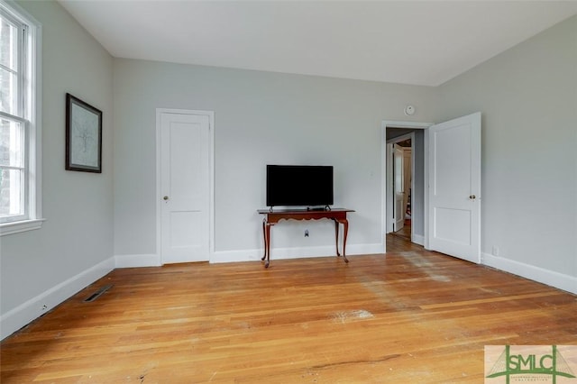 unfurnished living room featuring baseboards, light wood-type flooring, and a wealth of natural light