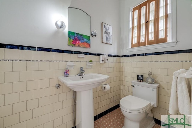 bathroom with tile patterned flooring, tile walls, toilet, and a wainscoted wall